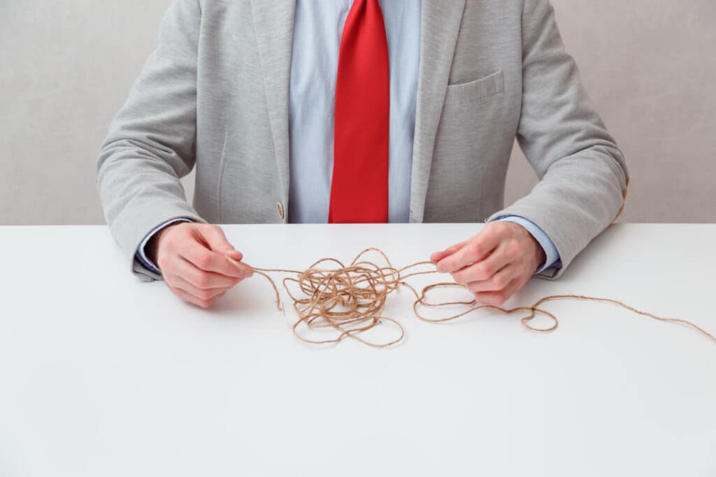 A lone businessman try to unwinds tangled thread ball like puzzle out situation. Conceptual photo. No face.