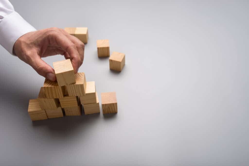 Businessman arranging wooden cubes in pyramid shape over grey background. With copy space on the right side of the image.