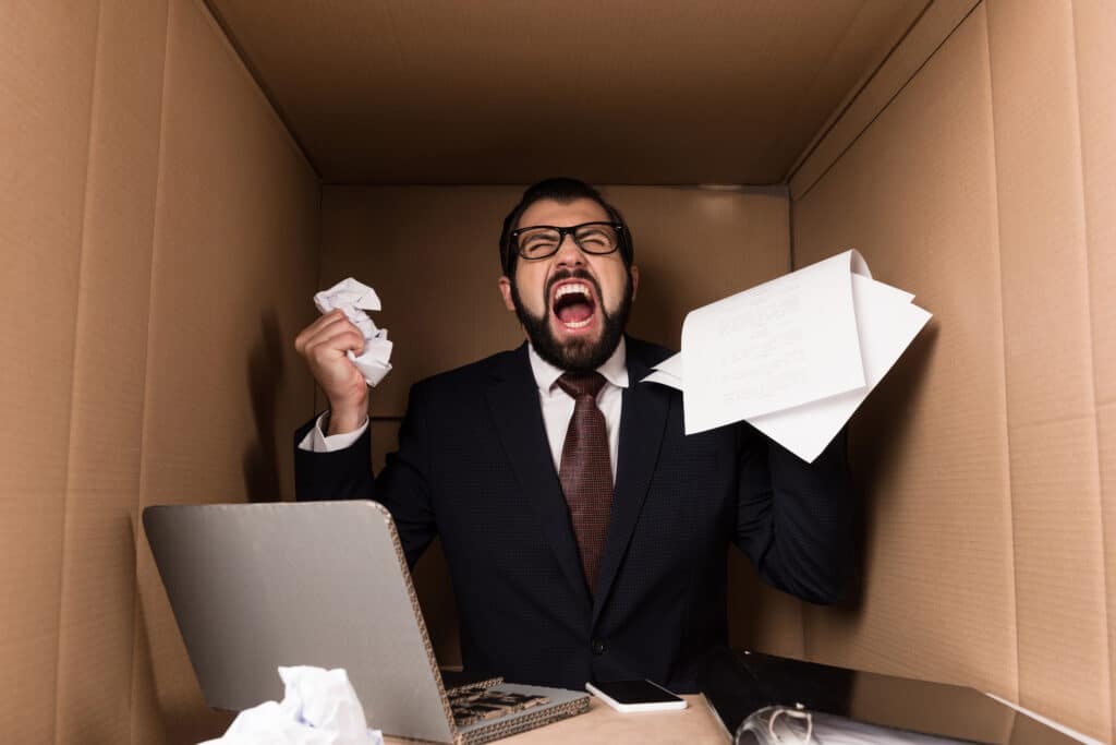angry businessman yelling and working with documents and cardboard laptop in box
