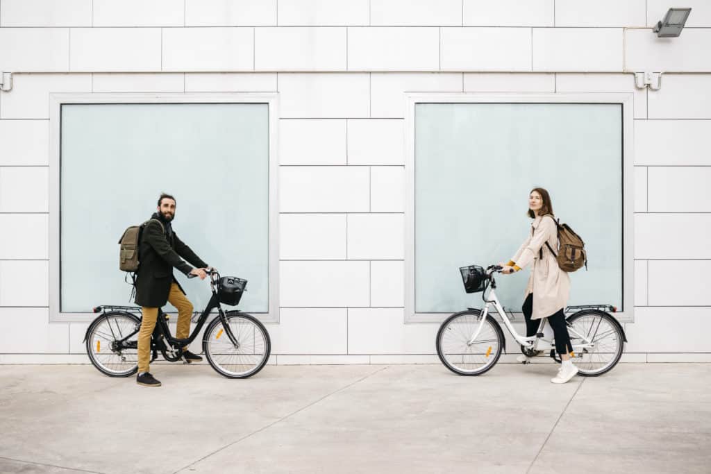 Portrait of man and woman with e-bikes standing at a building