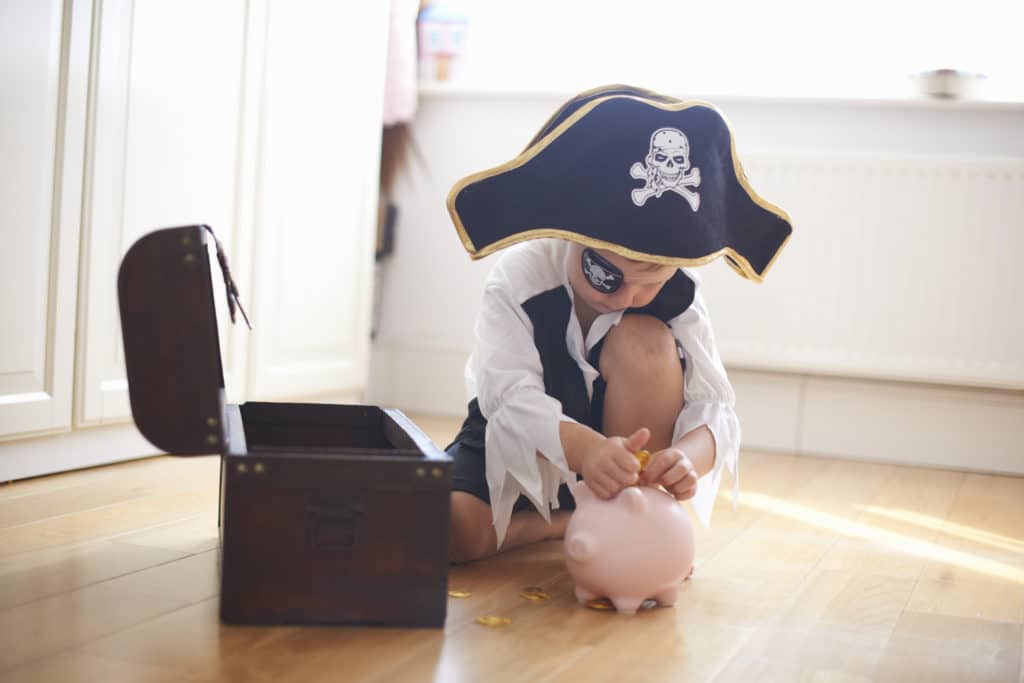 Young boy dressed as pirate, putting money into piggy bank