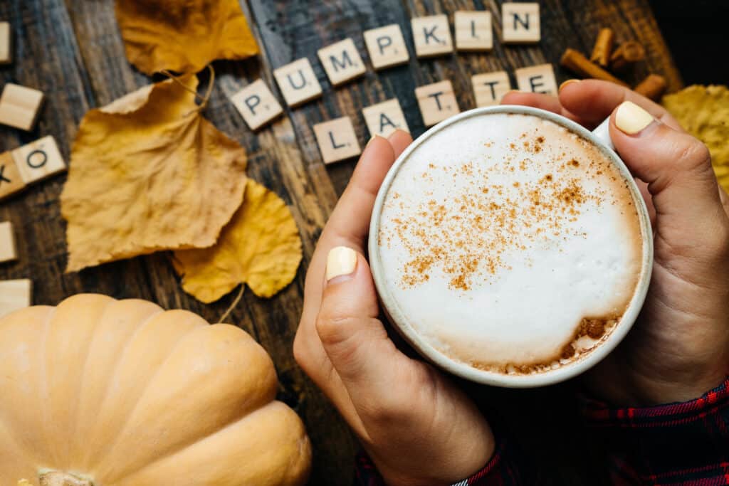 Closeup Pumkin latte wooden blocks against a rustic wood background with woman hands, coffee, pumpkins and autumn leaves