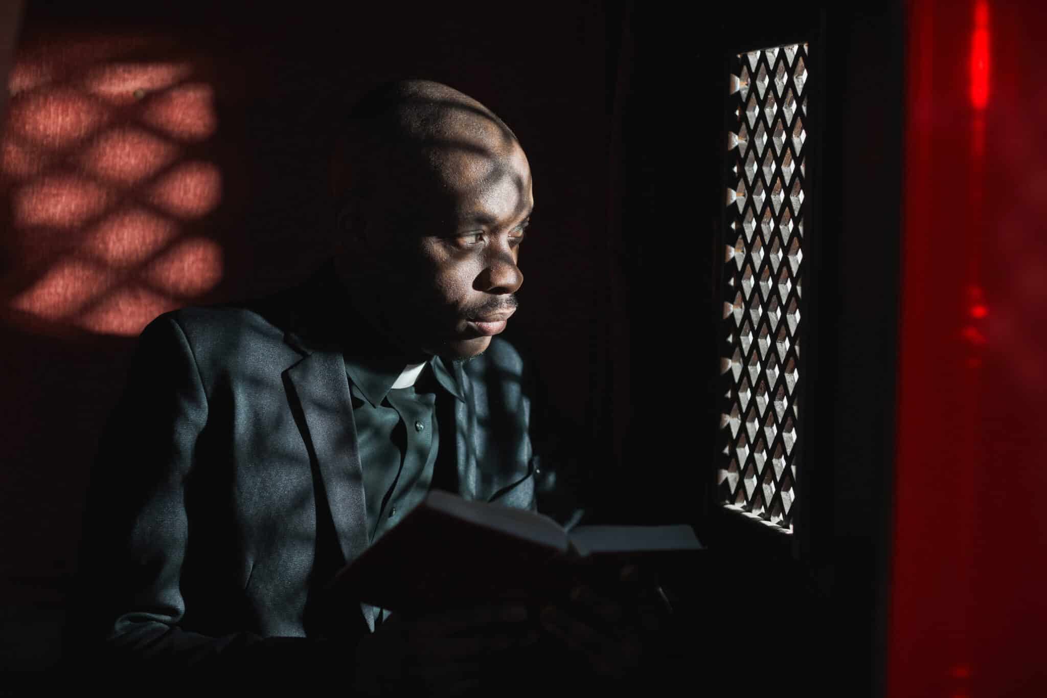 African priest reading the Bible while sitting in the confessional