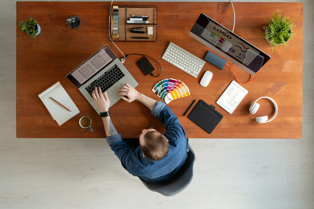 Directly above view of man with tattoo sitting at wooden table and editing ui design on laptop