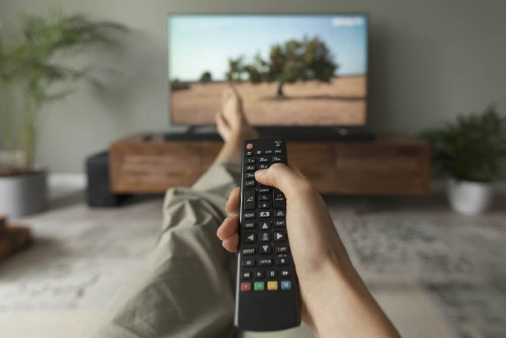 Woman watching TV on the couch at home and holding the remote control, point of view shot