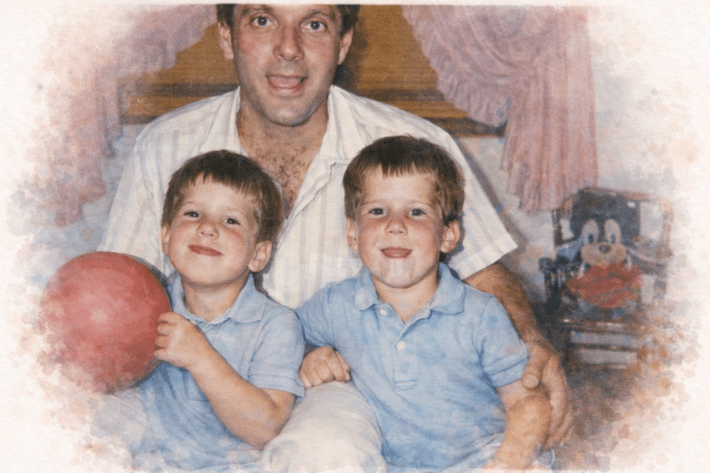 A man smiling with two young boys, both in blue shirts, sitting on his lap. One boy holds a red ball. In the background, there are pink curtains and a Mickey Mouse plush toy. The photo has a soft, painted effect.